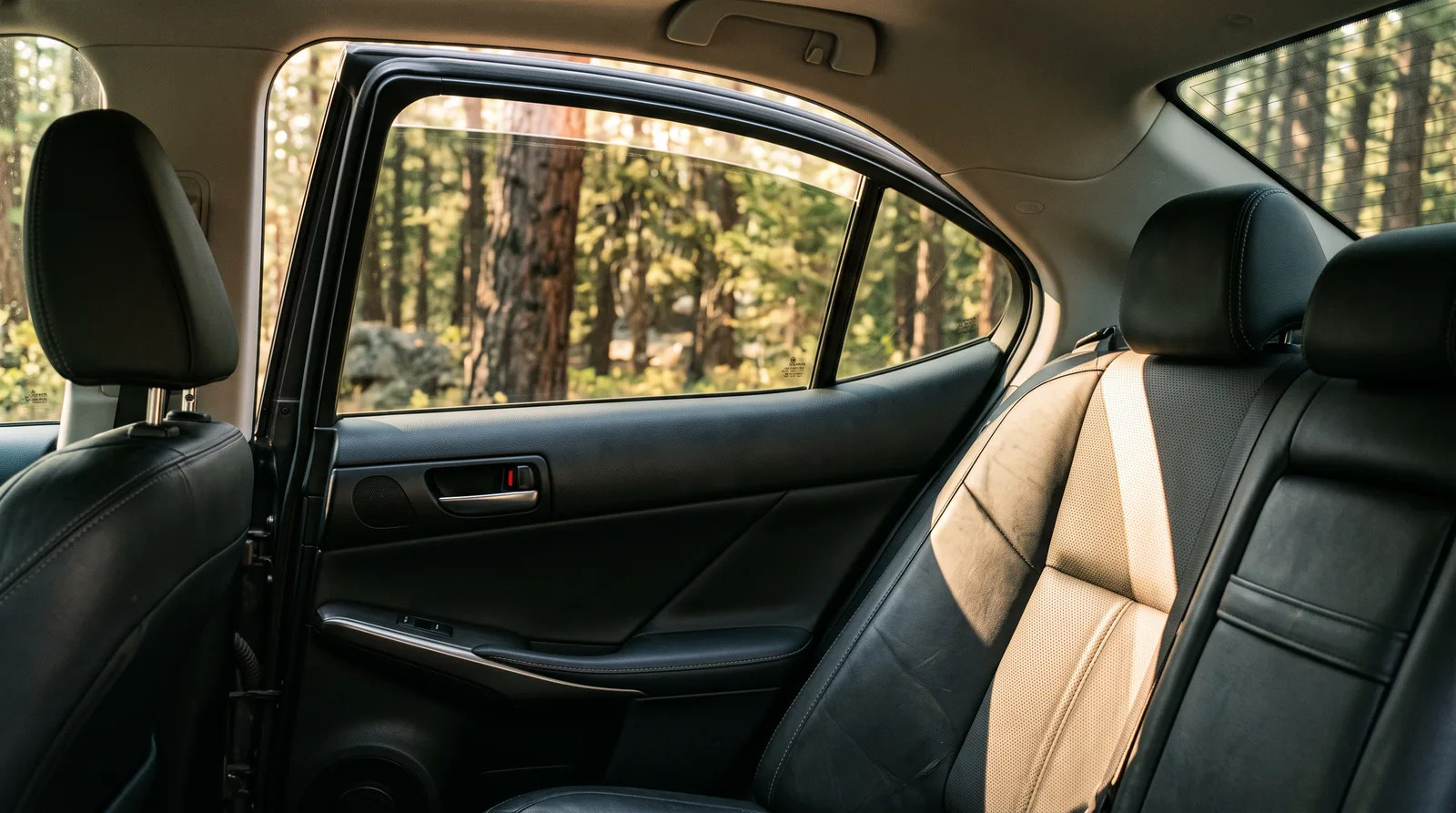 Afternoon sun shining through a car rear side window onto a black leather back seat, showing the solar heat that window tint heat rejection and IR rejection film are designed to block