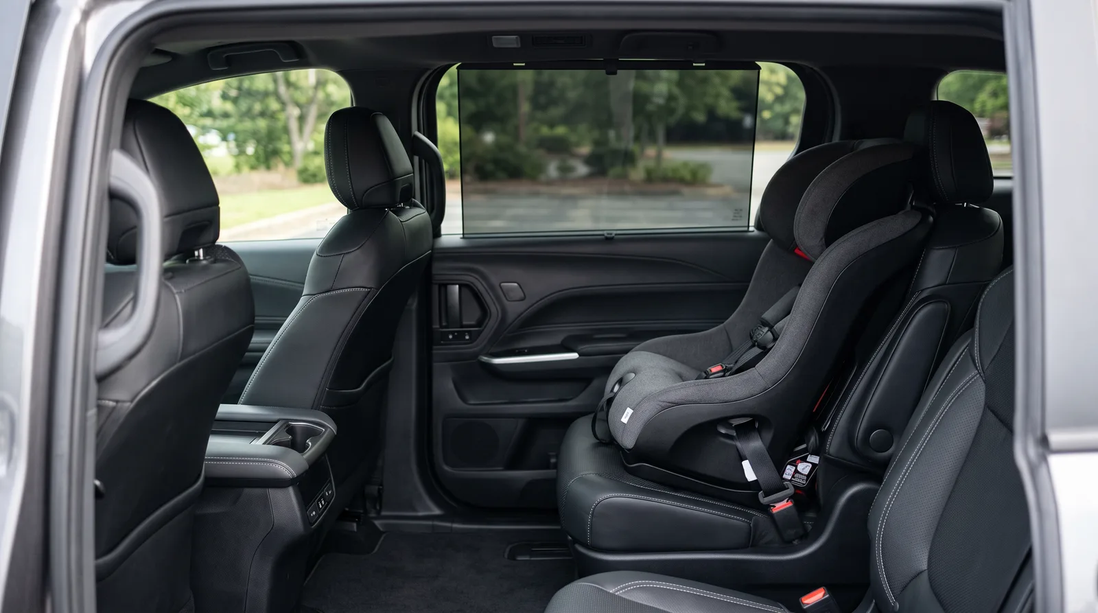 Empty child car seat in the second row of a family minivan beside sliding-door glass with a pull-up sunshade, showing the rear-seat sun exposure that window tint for a kid's car addresses