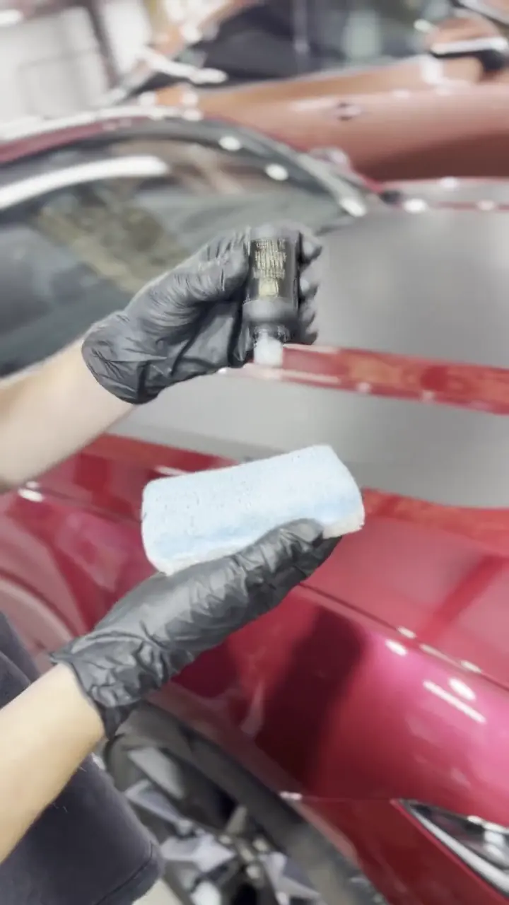 Gloved hands loading ceramic coating onto an applicator over a red Mustang hood