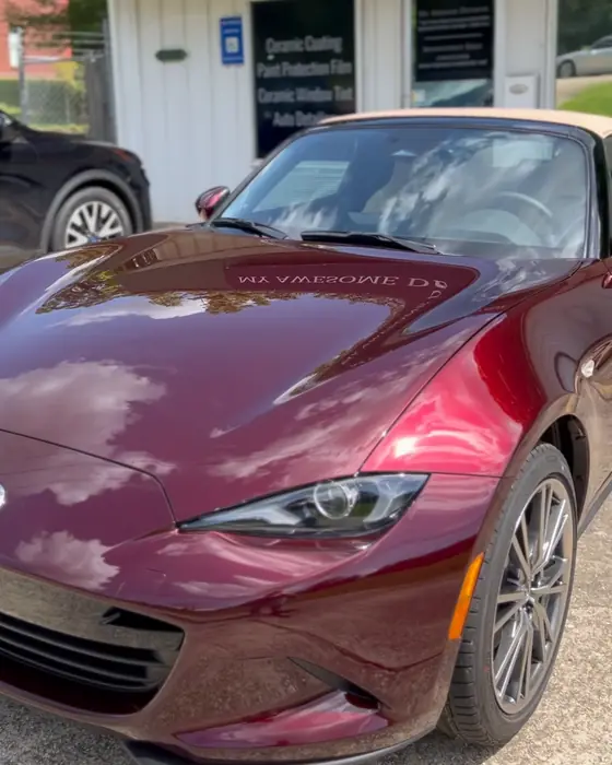 A burgundy Mazda MX-5 Miata parked in front of the My Awesome Detailer shop after ceramic coating