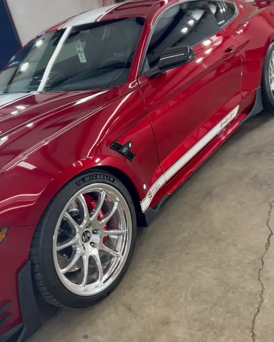 A red Mustang Shelby with white stripes and polished wheels in our shop after ceramic coating